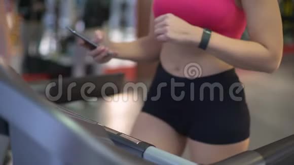 忙碌的年轻女性在健身房锻炼时使用小工具在跑步机上锻炼视频的预览图
