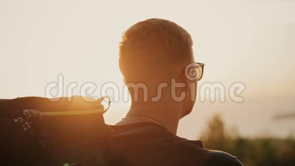 慢动作的英俊年轻时尚男子戴着太阳镜和背包看着夕阳在田野在一个视频的预览图