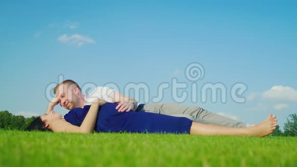 年轻的丈夫和怀孕的妻子在公园里放松一起躺在绿草上视频的预览图