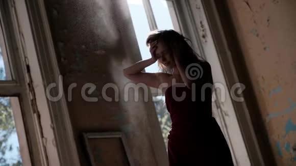 一个穿着红色长裙的年轻女子站在一座废弃的房子里站在灯光下表情迷人地抚摸着她的头发视频的预览图