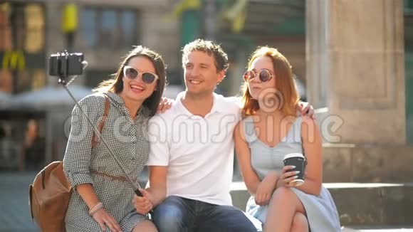 阳光明媚的夏日三位快乐的朋友在城市广场的智能手机户外自拍视频的预览图