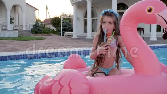 可爱的小女孩在泳池里尽情地亲吻孩子们在充气的火烈鸟上喝着甜饮料视频的预览图