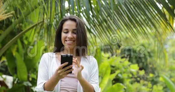 年轻女性用手机微笑在镜头中寻找户外女孩特写在绿树上聊天视频的预览图