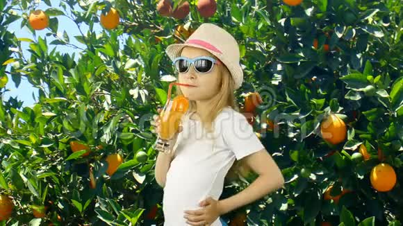 年轻的白种人女孩打开并在花园里喝橙汁和橘子树绿色花园夏日阳光明媚年轻视频的预览图
