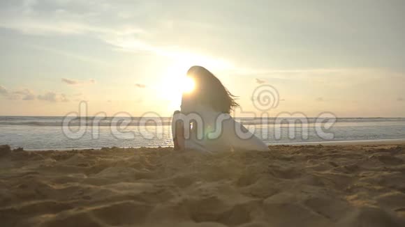 日落时分美丽的年轻女孩坐在海边坐在海边金色沙滩上的女人视频的预览图