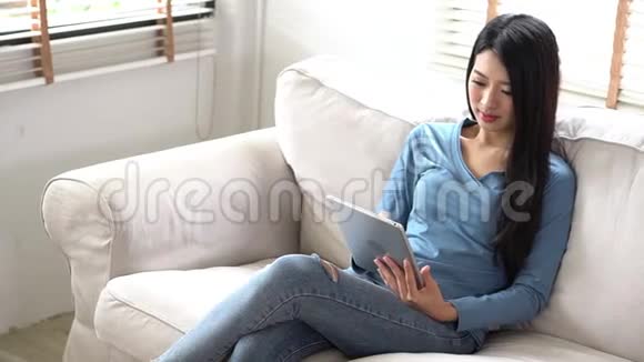 美丽的肖像年轻的亚洲女人微笑着快乐地使用数码平板电脑坐在客厅的沙发上视频的预览图