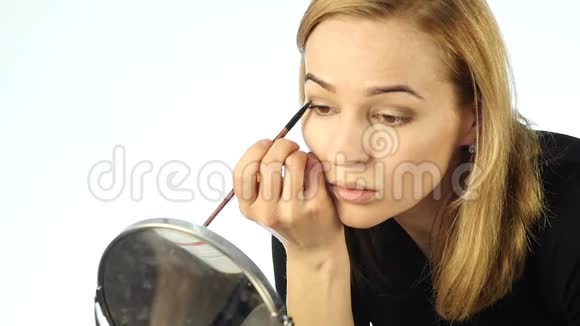 美丽的金发女人每天在镜子前化妆用小刷子画眉毛慢动作视频的预览图