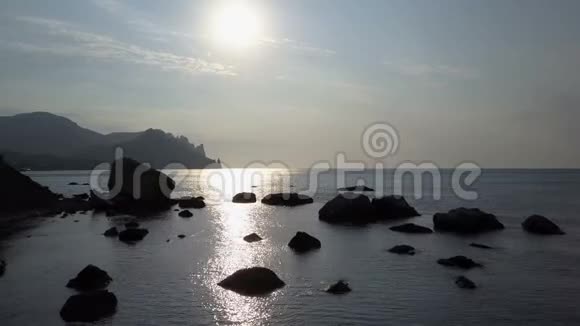 日出时带着岩石和石头向后飞越海面山岩石水和海中的石头视频的预览图
