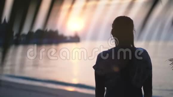 美丽的夕阳下站在海滩上的女人的剪影视频的预览图