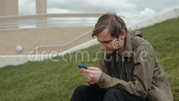 休闲快乐的男人用智能手机坐在草地上的公园学生的长凳上视频的预览图