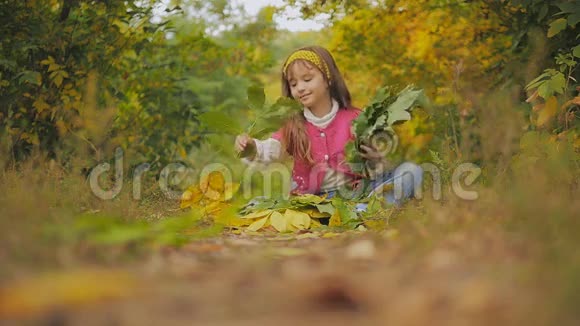 开朗的女孩坐在步道上扔秋叶慢动作视频的预览图