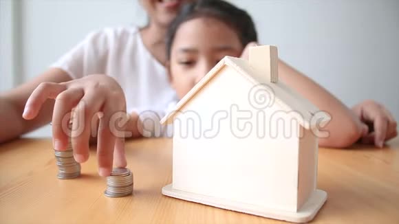 4妈妈和亚洲小女孩把钱币放在房子里储蓄罐选择集中在房子里视频的预览图