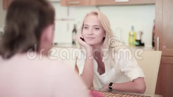 漂亮的金发女郎和穿白衣服的年轻人正坐在厨房的桌子旁视频的预览图