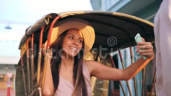 泰国老城区骑自行车车夫出租车的年轻混血旅游女孩用手机拍照视频的预览图