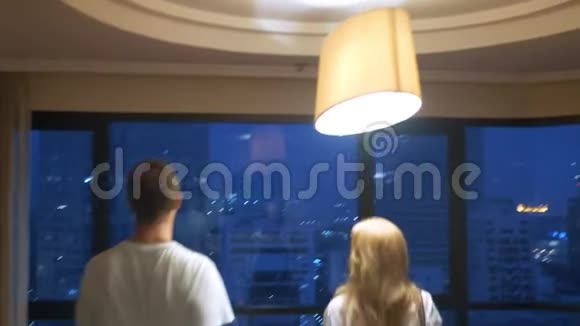 一对漂亮的夫妇一个女人和一个男人带着一个手提箱在摩天大楼的背景下在傍晚的全景窗口里视频的预览图