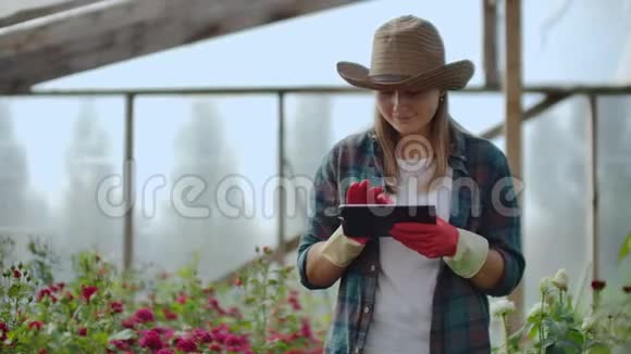 美女花商拿着平板电脑在温室里走来走去查看种植的玫瑰记录下视频的预览图