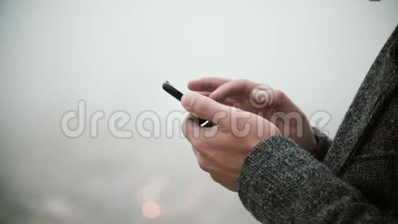 近距离观看男性手拿手机与触摸屏在雾蒙蒙的公园里用智能手机的年轻人视频的预览图