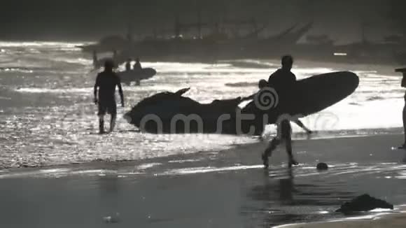 日落时分带着冲浪板在热带海滩上行走的不可辨认的年轻人的剪影海景美景视频的预览图