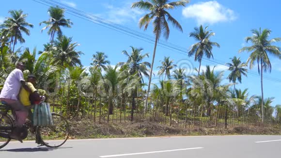 在阳光明媚的日子里印度父亲和儿子骑着自行车沿着热带国家的沥青路亚洲家庭自行车赛道视频的预览图