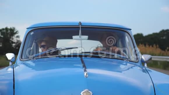 年轻夫妇戴着帽子乘着老式汽车在夏季旅行男人和女人坐在旧复古车的前座视频的预览图