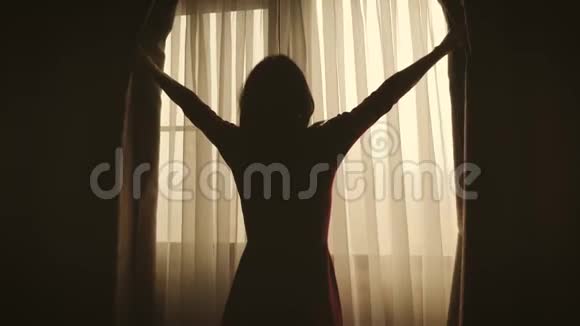 可爱的女孩醒着站在窗前美丽的女人打开窗帘透过窗户看视频的预览图