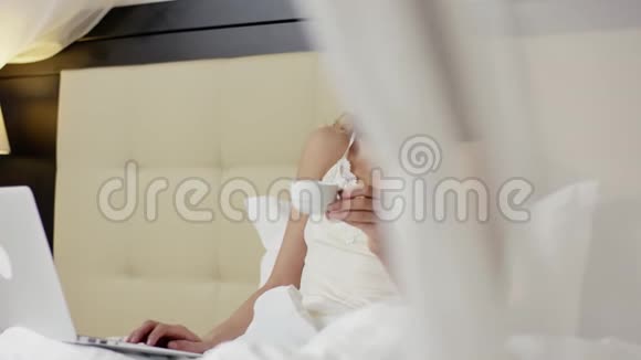 女人躺在床上喝咖啡在笔记本电脑上进行视频对话视频的预览图