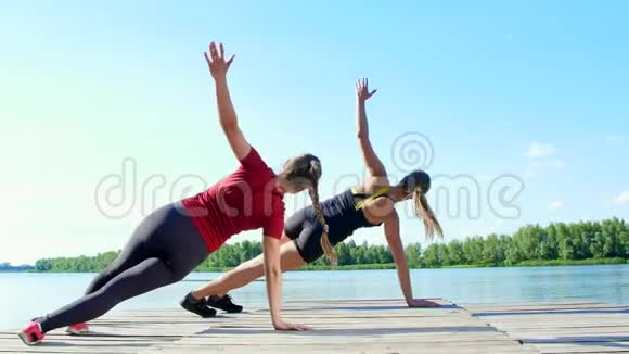 两个漂亮的运动的金发女人同步做协调和平衡练习湖泊河流蓝天视频的预览图
