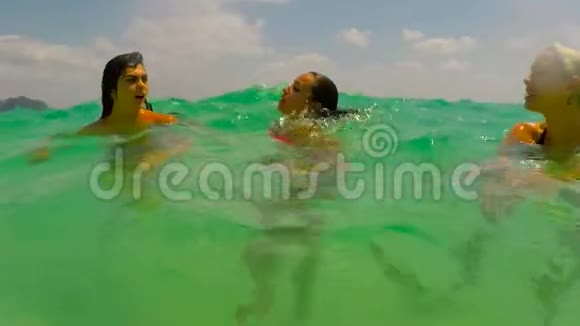 三个女孩在海里游泳在美丽的海滩上年轻女子在蓝色的海水中交谈的镜头镜头视频的预览图