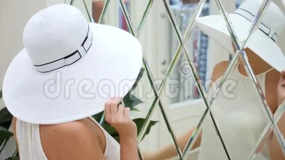 一个戴着白色大帽子和白色连衣裙的女人看着镜子4k慢动作视频的预览图
