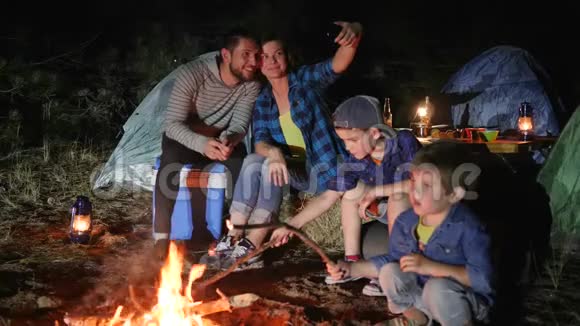 幸福家庭在森林篝火附近的手机上拍照带着孩子的父母进入旅游营地拍照视频的预览图