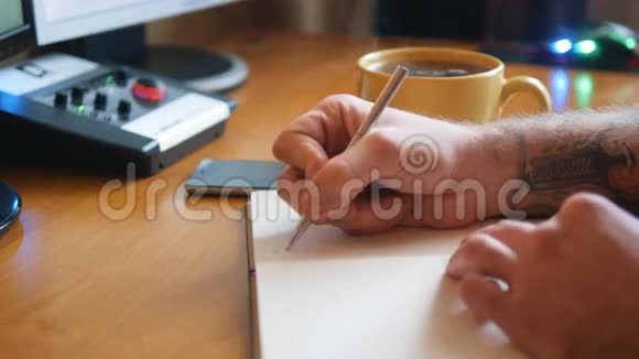 在笔记本上用文身书写的男性手电话和一杯咖啡放在桌上视频的预览图