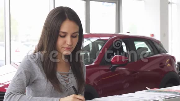年轻有魅力的女司机在汽车经销店填写文件视频的预览图