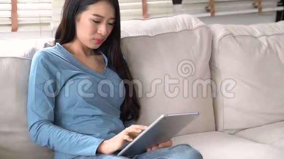 美丽的肖像年轻的亚洲女人微笑着快乐地使用数码平板电脑坐在客厅的沙发上视频的预览图
