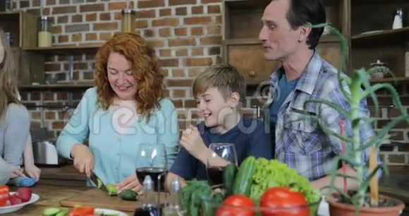 幸福的家庭帮助母亲一起在厨房做饭父母带着两个孩子在家吃饭视频的预览图