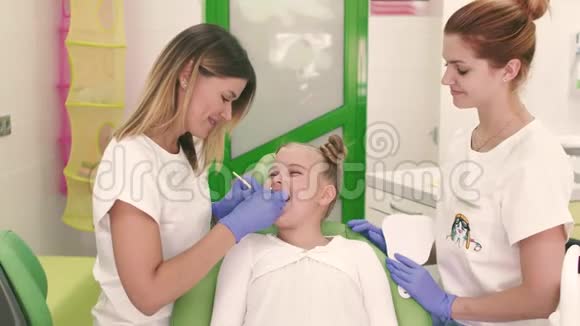 坐在牙科椅上的小女孩牙医和她的助手在看牙齿他们都在微笑视频的预览图
