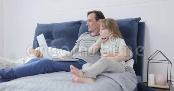 家庭在卧室使用平板电脑和笔记本电脑快乐的父母在家陪伴孩子视频的预览图