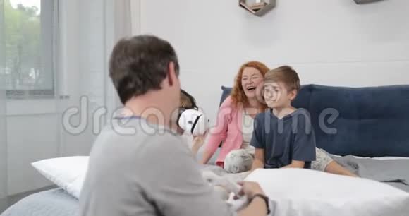 幸福的家庭在卧室里看着小女孩尝试虚拟现实的眼镜父母带着孩子一起晨曦视频的预览图
