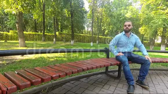 有胡子的快乐男人坐在公园里吃东西视频的预览图
