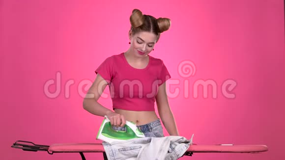 青少年在粉红色的木板上用熨斗熨烫衣服粉色背景视频的预览图