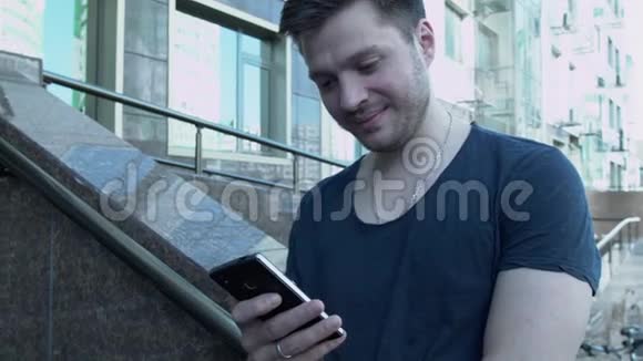有人在打电话一个有智能手机的年轻人在大楼附近写短信一个穿T恤的英俊青年视频的预览图