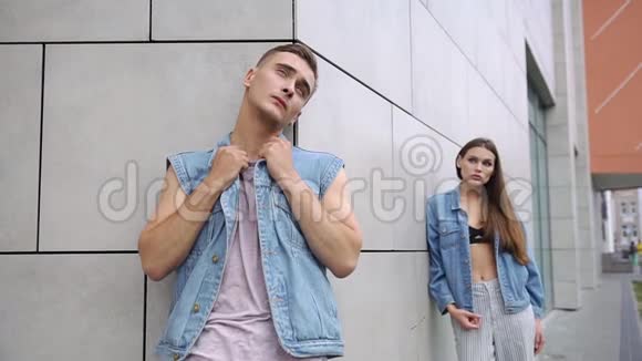 一位留着长发的女人站在一个穿着牛仔裤夹克的男人的身后站在灰色的墙壁前视频的预览图