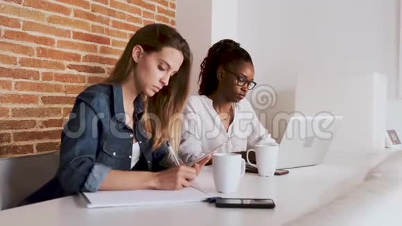 两位年轻漂亮的商务女性在办公室里用数码平板电脑和笔记本电脑工作视频的预览图