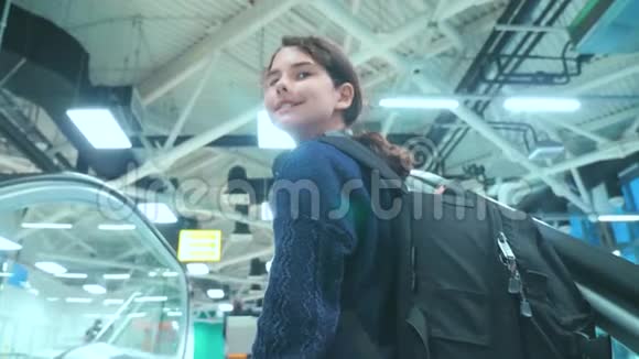 年轻的旅游女孩带着背包带着手提箱沿着自动扶梯向上移动机场等待飞机的生活方式视频的预览图