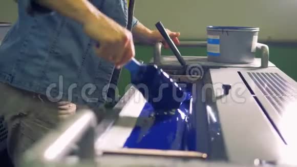 一名雇员在一台工业印刷机上准备蓝色油漆视频的预览图