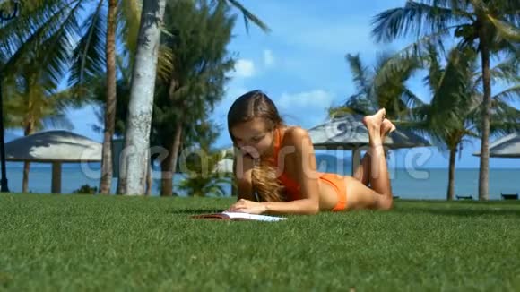 穿橙色泳装的女孩在草坪上阅读书籍视频的预览图