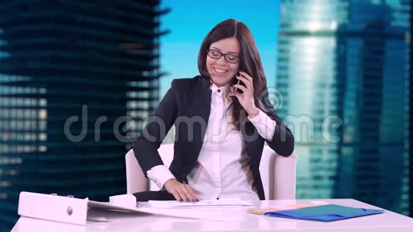 商务女性坐在办公室的办公桌前微笑着在电话里交谈桌子上有文件和合同视频的预览图
