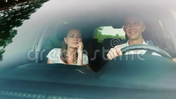 一对年轻夫妇正坐汽车旅行从挡风玻璃上看它反映了树木和运动的景色视频的预览图
