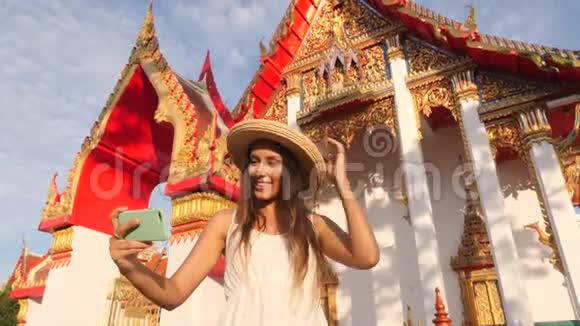 穿着白裙戴着大草帽的年轻混血旅游女孩在泰国用手机拍照视频的预览图