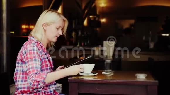 一个年轻的女人坐在一家舒适的咖啡馆的桌子旁使用平板电脑奥地利格拉茨市视频的预览图