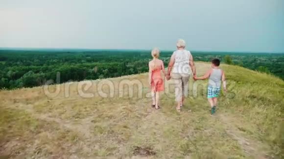 祖母手里拿着两个孙子一个女孩和一个男孩走过热闹的农村回去视频的预览图